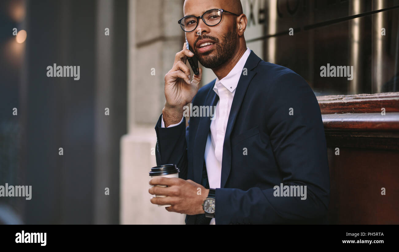 Ritratto di bel giovane imprenditore facendo una telefonata mentre seduti all'aperto con un caffè. Uomo in business suit parlando su telefono cellulare. Foto Stock