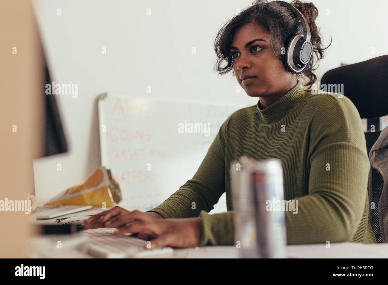 Programmatore femmina lavorando in una via di sviluppo software ufficio della compagnia. Donna che indossa le cuffie codifica su computer desktop. Foto Stock