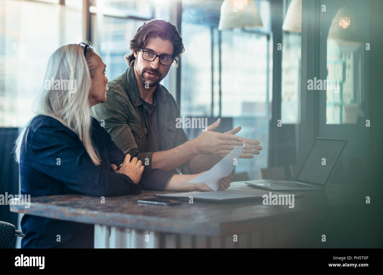 Giovane uomo spiegando la sua idea di business a femmina matura collega di lavoro. La gente di affari avente una riunione per la discussione del progetto. Foto Stock