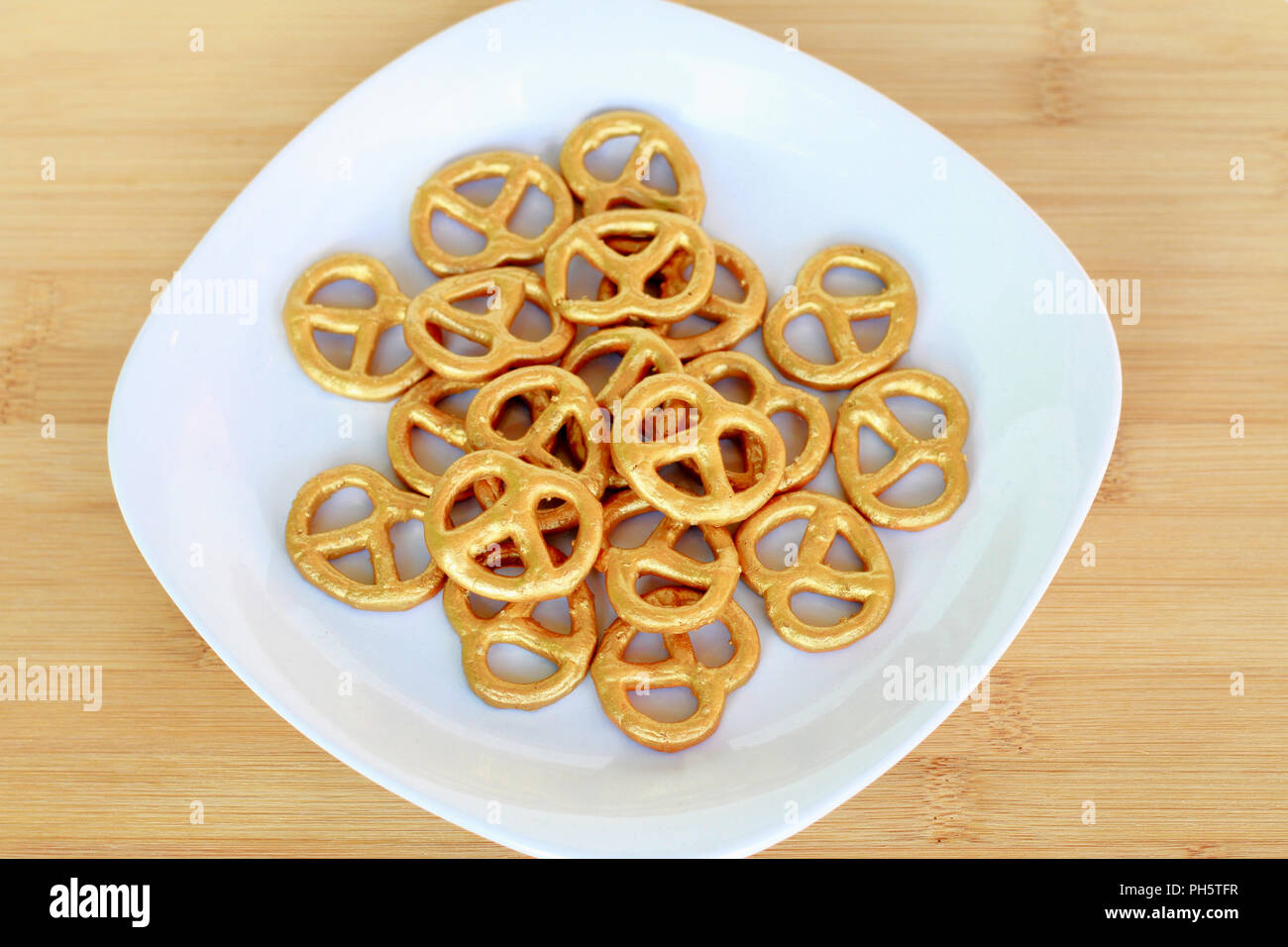 Una piastra d'Oro dipinta pretzel si appoggia su una tavola di legno. Foto Stock