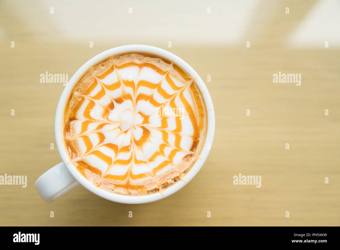 A caldo il caffè macchiato con caramello in tazza bianca sulla tavola di legno dalla luce della finestra, Tabella vista superiore Foto Stock