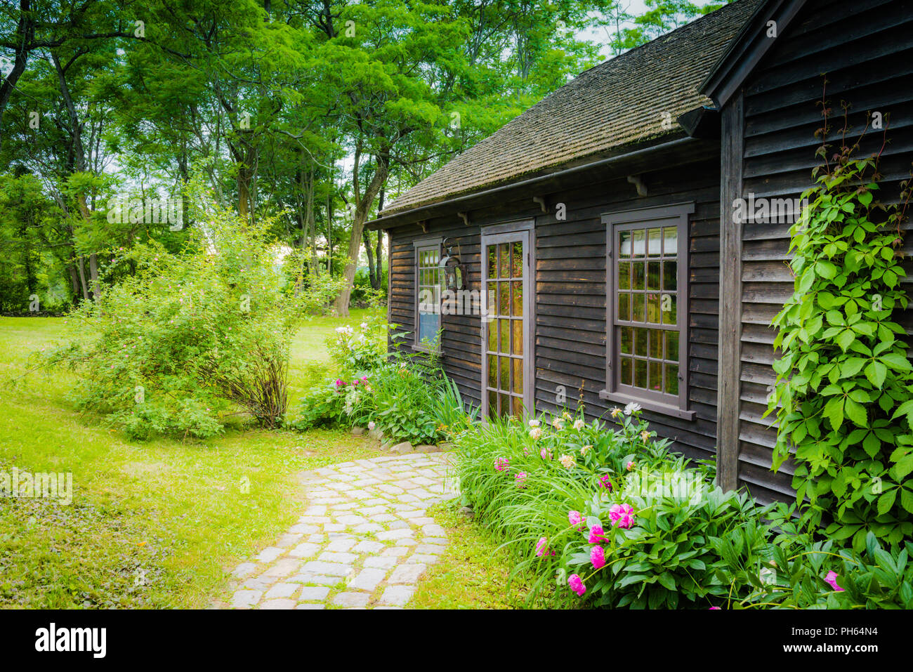 Un cottage di legno circondato da frontiere perenne e alberi di alto fusto in Upstate New York. Foto Stock