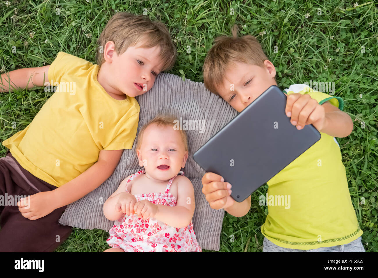 I bambini tenere ipad nelle loro mani sdraiati sull'erba. Foto Stock