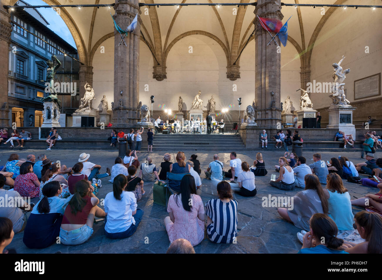 Firenze, Italia - 2018, 14 Luglio: Gente seduta sul pavimento della Piazza della Signoria, durante un open-air concerto presso la Loggia dei Lanzi. Foto Stock