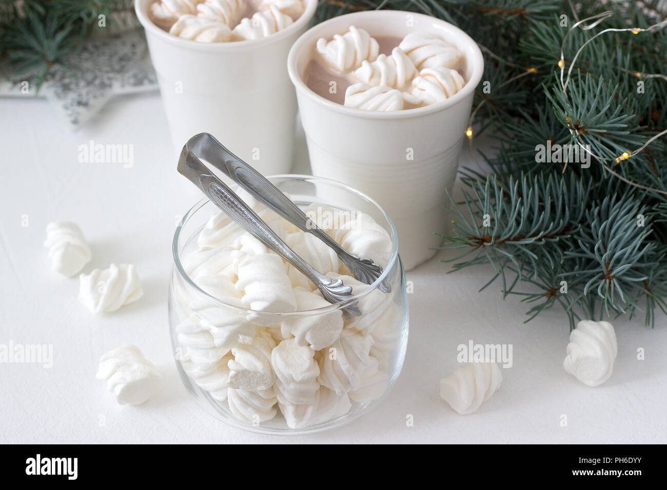 Il cacao con marshmelow in bianco tazze e marshmallows in un vasetto di vetro su un tavolo bianco con rami di abete e la ghirlanda. Foto Stock