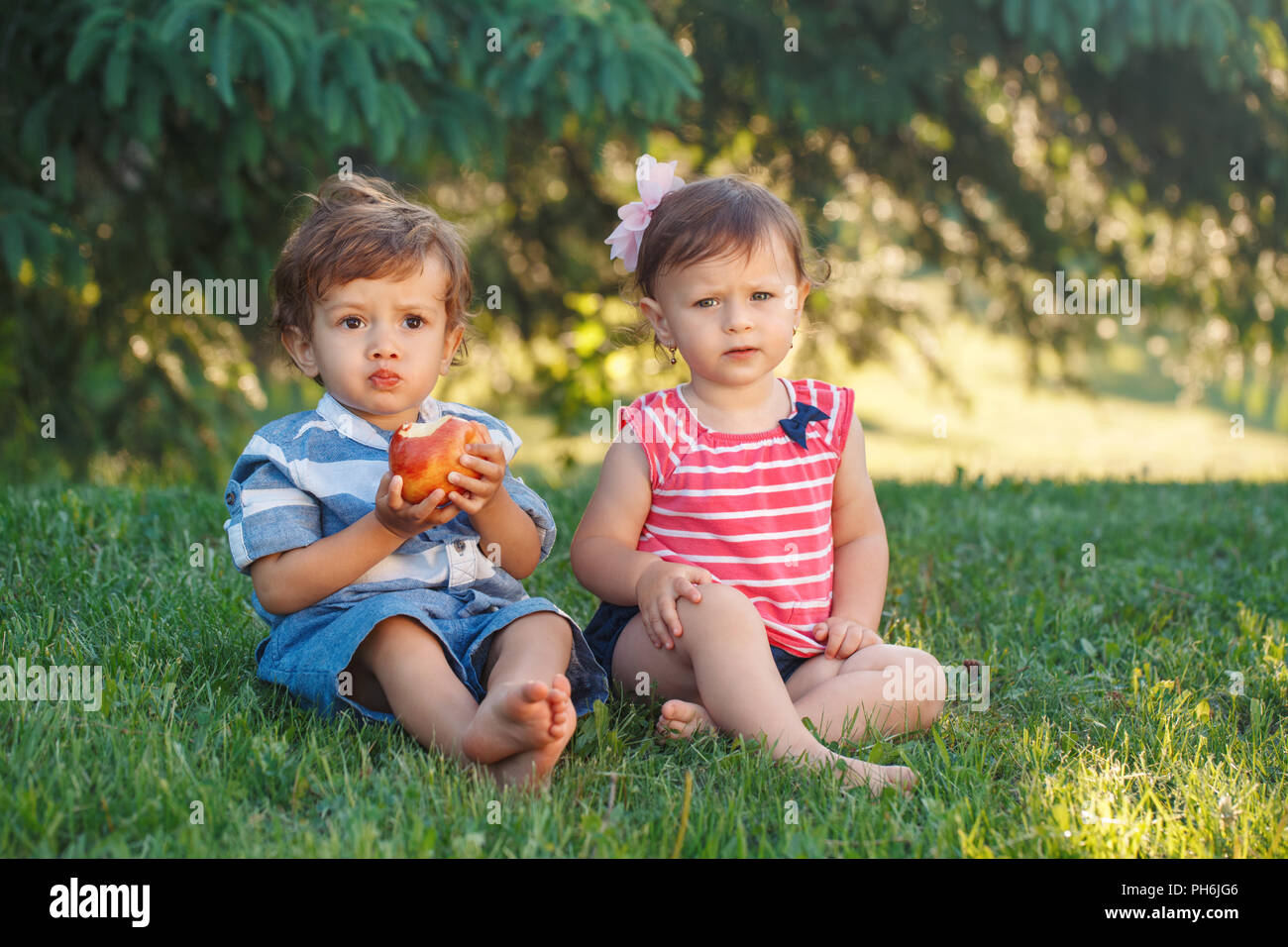 Ritratto di gruppo di due white Caucasian carino divertente adorabili bambini bambini seduti insieme condividendo cibo apple. Invidia amicizia concetto di infanzia. Essere Foto Stock