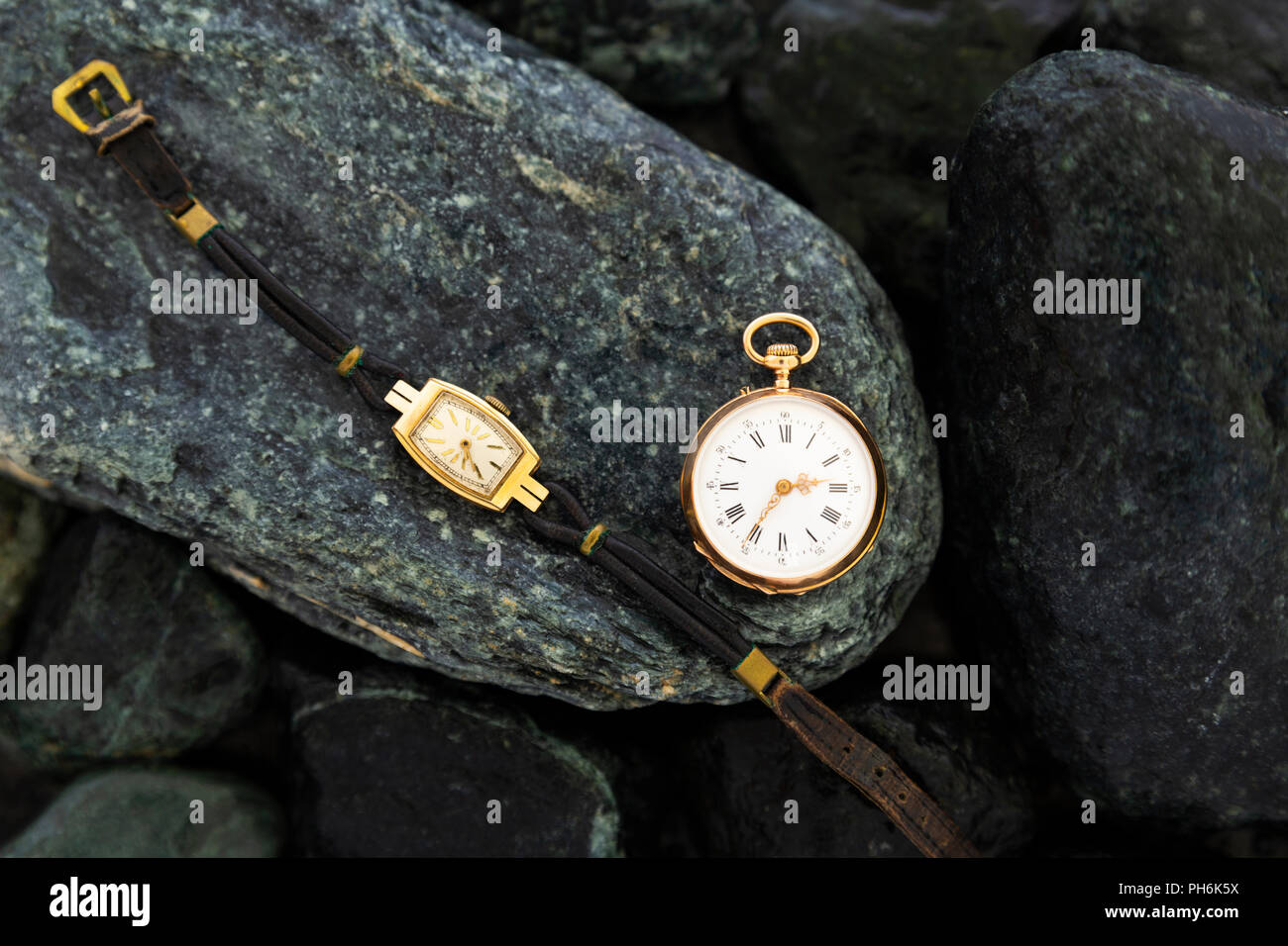 Set di orologi su bagnato pietre verdi con un classico oro orologio da tasca e un orologio da polso con usura cinghie in pelle Foto Stock