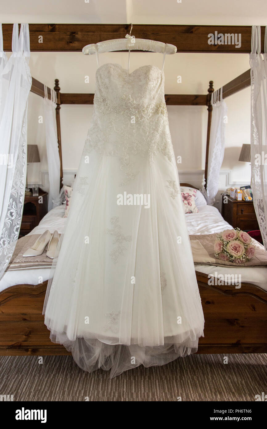 Abito da sposa appeso su un letto a baldacchino in attesa di essere indossato da una sposa il giorno delle nozze, prese alla luce del giorno in una camera da letto Foto Stock