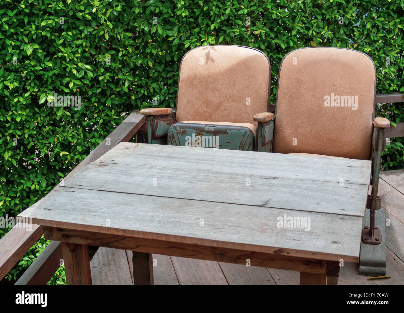 Teatro Vintage posti a sedere con tavoli in legno sulla terrazza in legno sulla macchia verde dello sfondo. Mix unico e abbina arredamento in stile concetto. Foto Stock