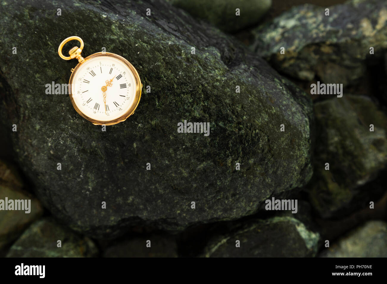 Primo piano di un bellissimo oro classico orologio da tasca la posa su bagnato pietre verdi Foto Stock