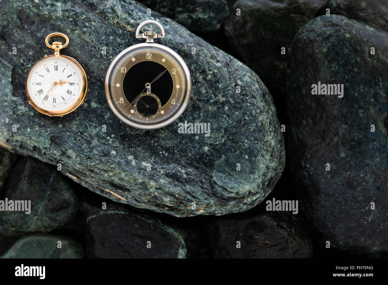 Set di orologi su bagnato pietre verdi con un classico oro orologio da tasca e un nero e argento orologio da tasca Foto Stock