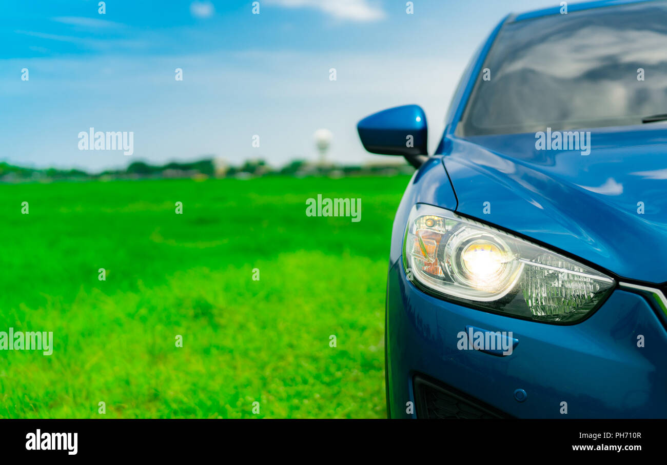 Vista frontale del lusso blu compatte auto SUV con lo sport e il design moderno parcheggiato su erba verde campo con cielo blu e nuvole bianche. Auto ibride e aut Foto Stock