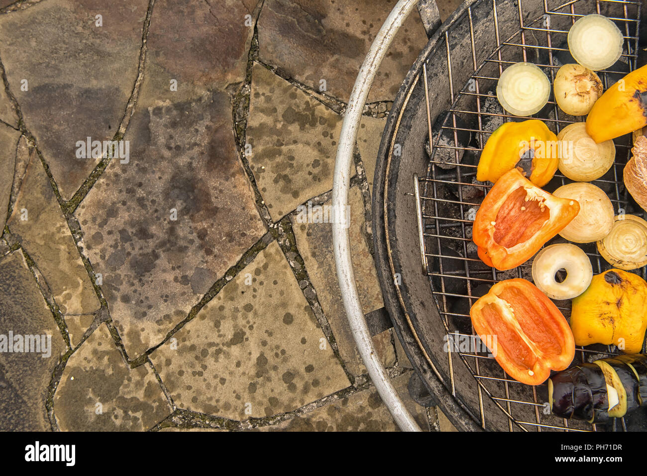 Assortimento di verdure grigliate sulla griglia metallica di round grande grill esterno permanente sulla pietra naturale pavimentazione. Mangiare sano concetto. Messa a fuoco selettiva Foto Stock