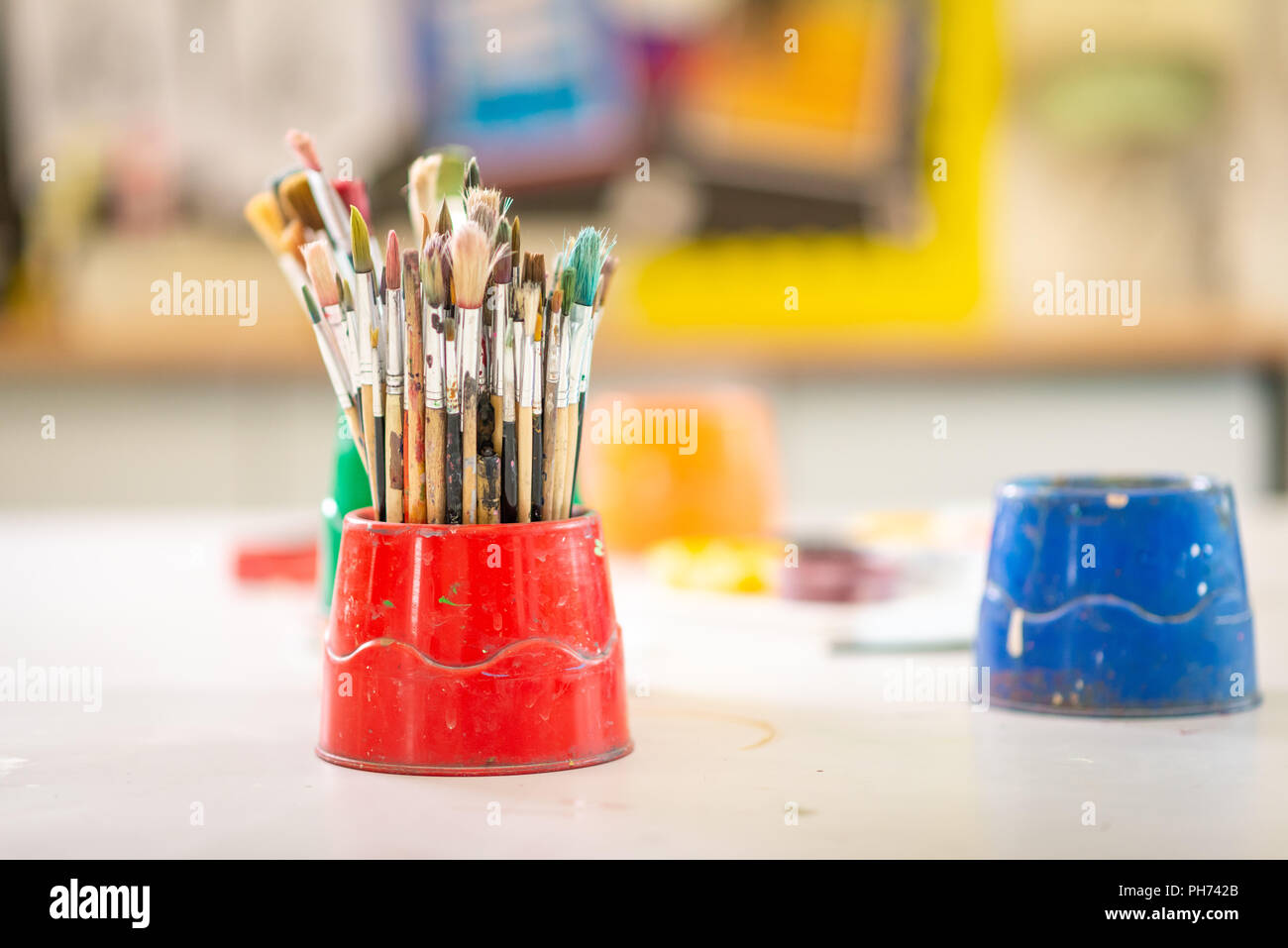 Pentole di artista della vernice usata spazzole su un banco di scuola fotografata nella scuola d'arte Foto Stock