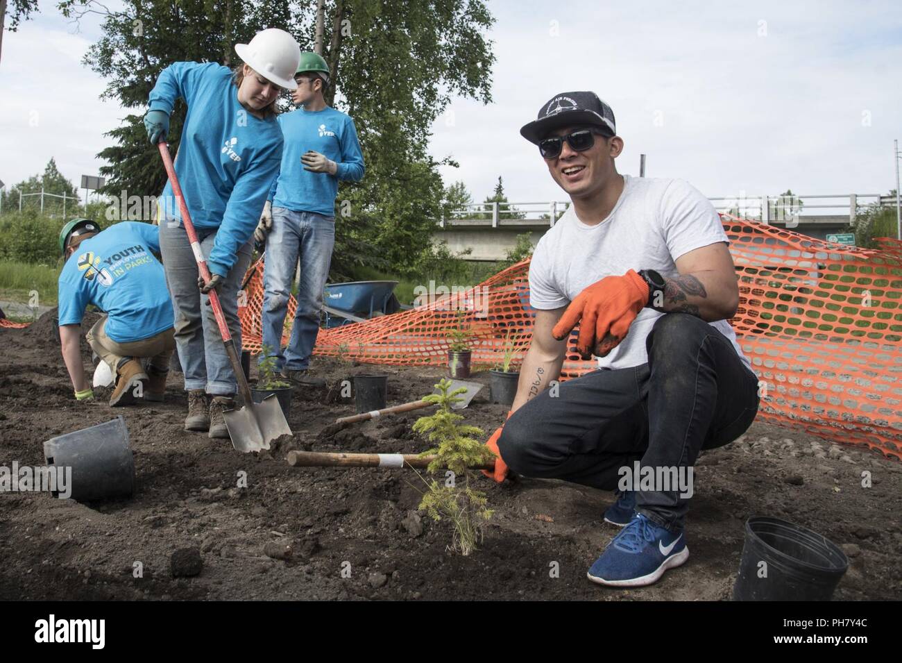 Stati Uniti Air Force Staff Sgt. Mario Perez, un Pacific Air Forces' F-116 dimostrazione avionica Team specialista, scava buche per bulbi per alberi con l'occupazione giovanile nei parchi membri del programma in Anchorage in Alaska, 29 Giugno, 2018. La demo team hanno lavorato insieme per piantare più di trenta alberelli, che aiuti a rafforzare argini. Foto Stock