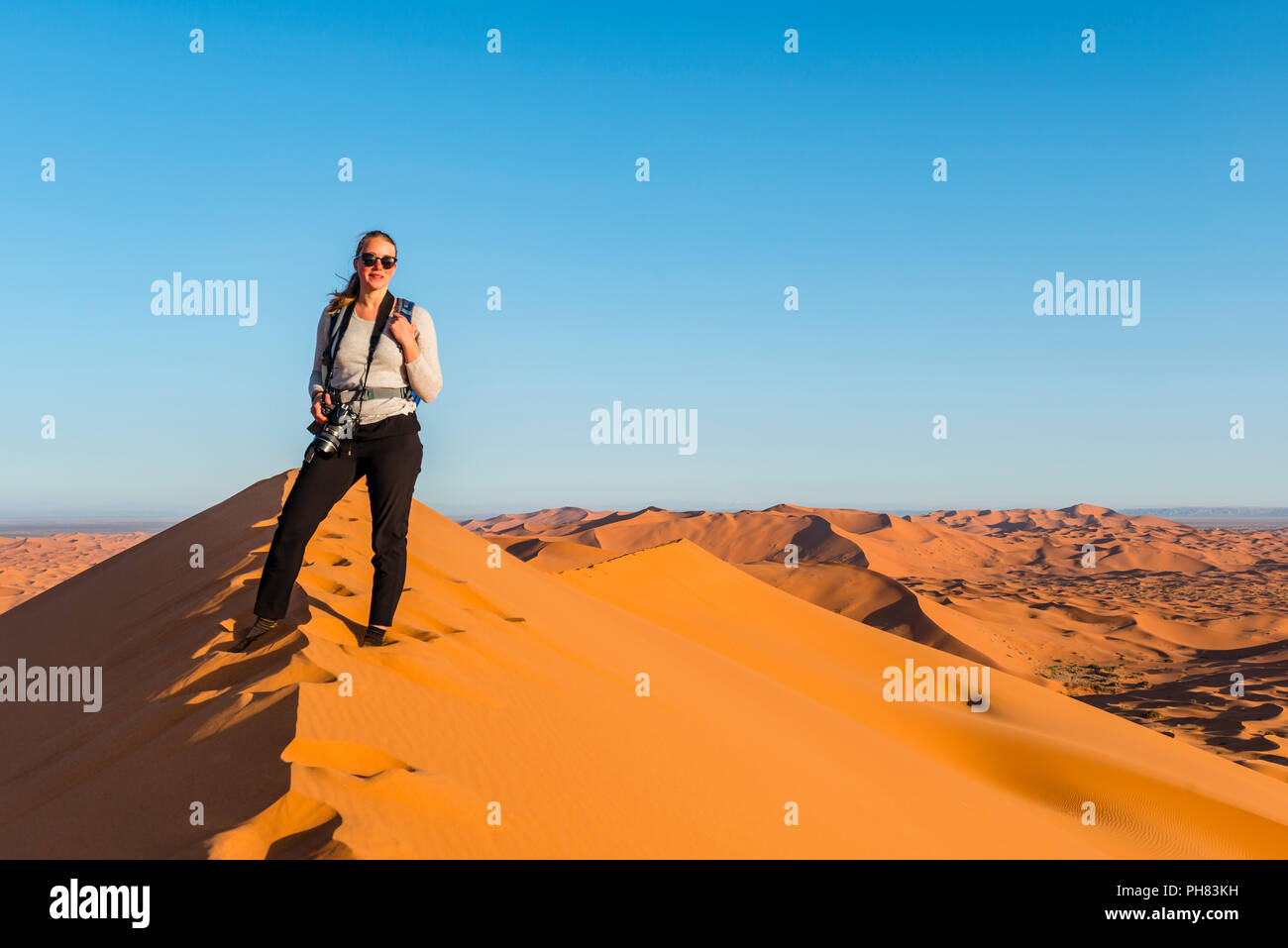 La donna si erge su un dune di sabbia rossa nel deserto, paesaggio di dune Erg Chebbi, Merzouga, Sahara, Marocco Foto Stock