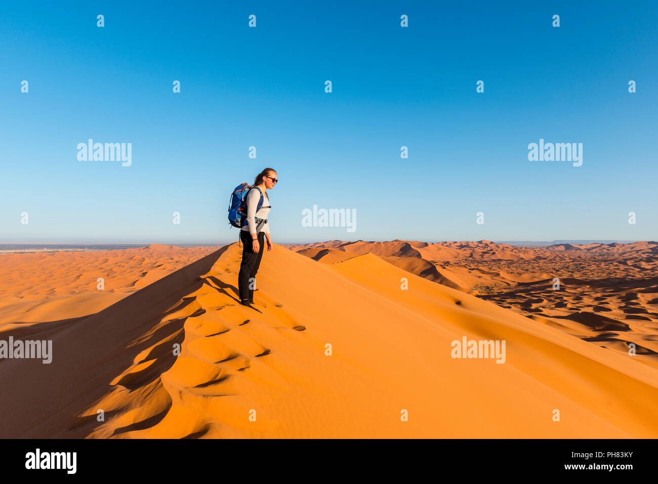 La donna si erge su un dune di sabbia rossa nel deserto, paesaggio di dune Erg Chebbi, Merzouga, Sahara, Marocco Foto Stock