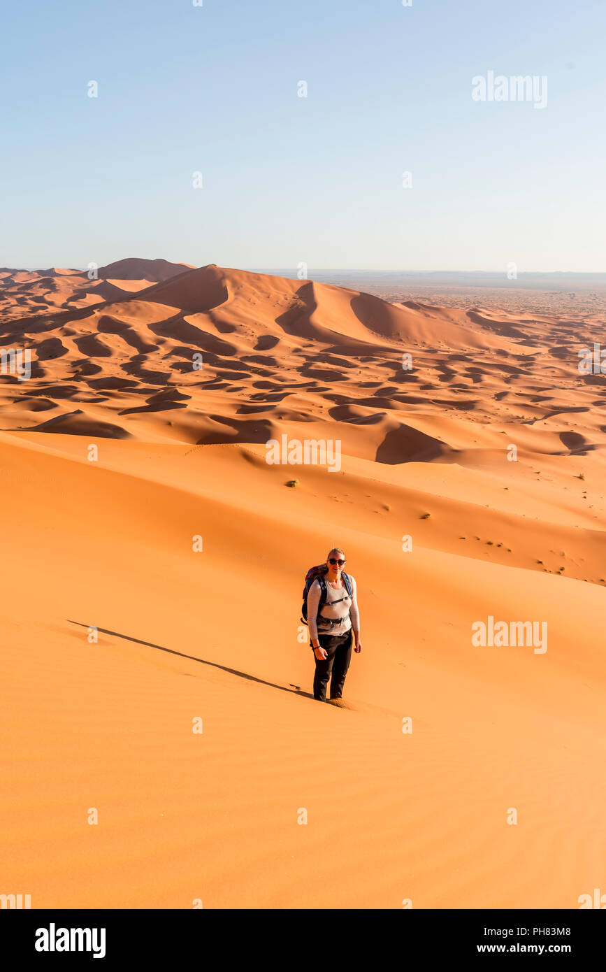 La donna sta nella sabbia sulle dune, dune di sabbia rossa nel deserto, paesaggio di dune Erg Chebbi, Merzouga, Sahara, Marocco Foto Stock