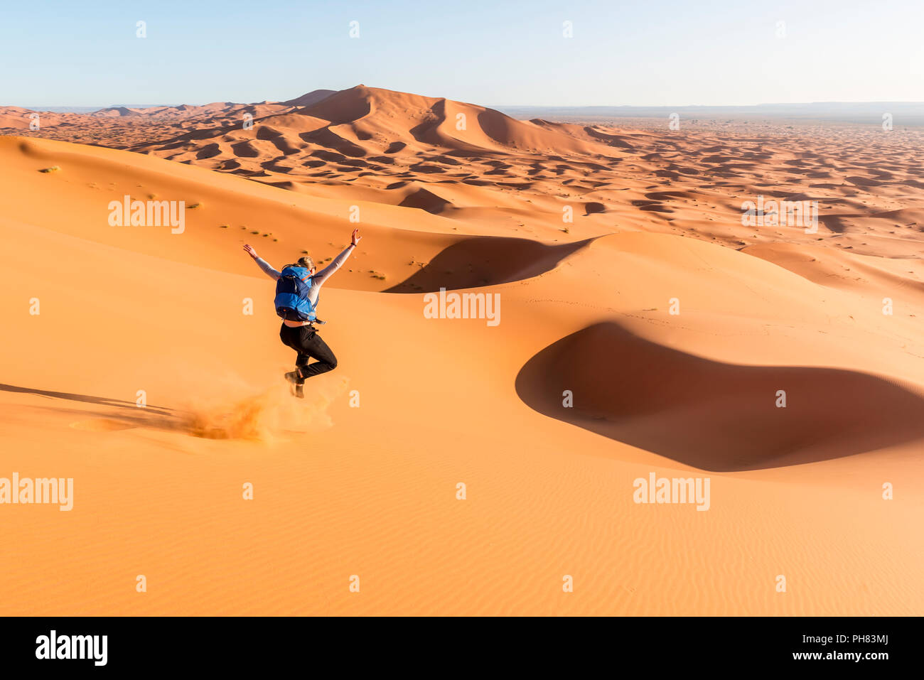 Donna in corsa in discesa, dune di sabbia rossa nel deserto, paesaggio di dune Erg Chebbi, Merzouga, Sahara, Marocco Foto Stock