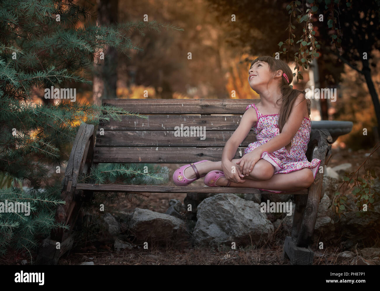 Piccola ragazza seduta su una panchina Foto Stock