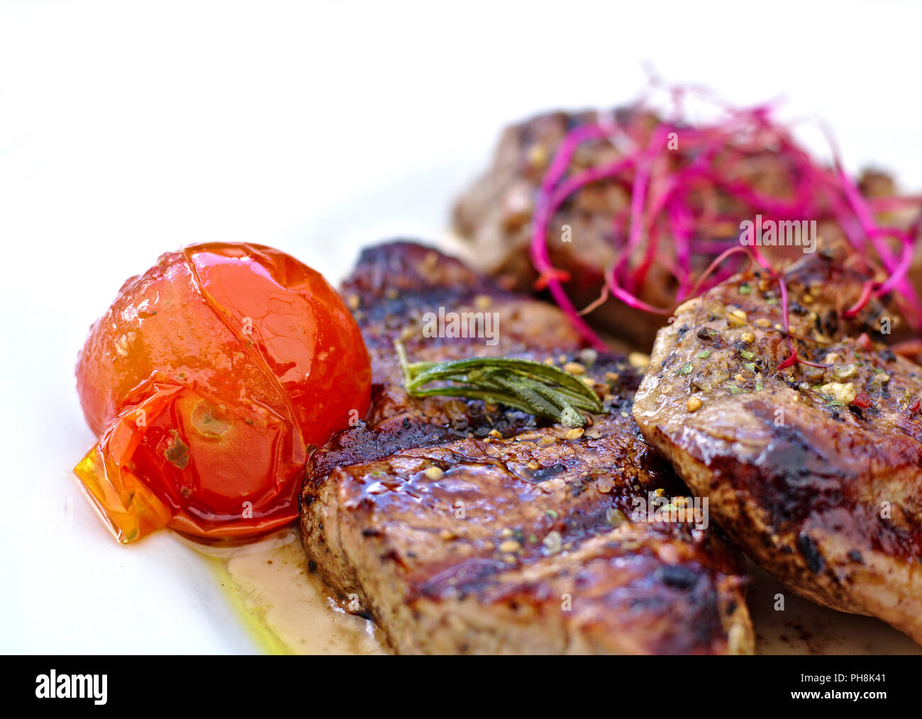 Tre bistecche con arrosti di pomodoro e pezzi di rosa e insalata verde su una piastra bianca Foto Stock