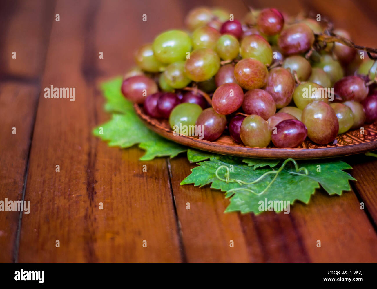 Uva su una piastra di argilla su tavole di legno .ancora in vita con rosa moscato. Foto Stock