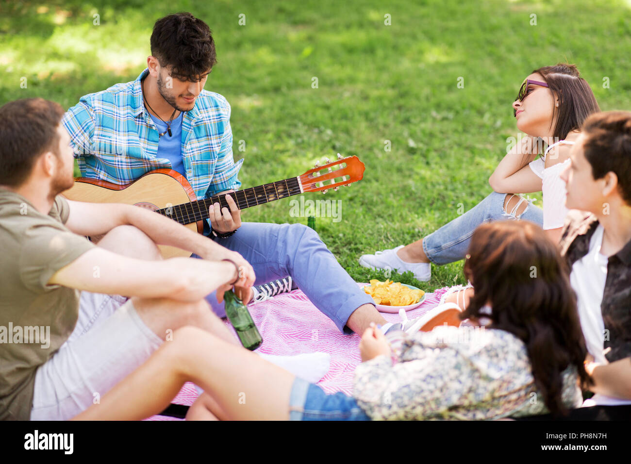 Amici a suonare la chitarra al picnic nel parco di estate Foto Stock