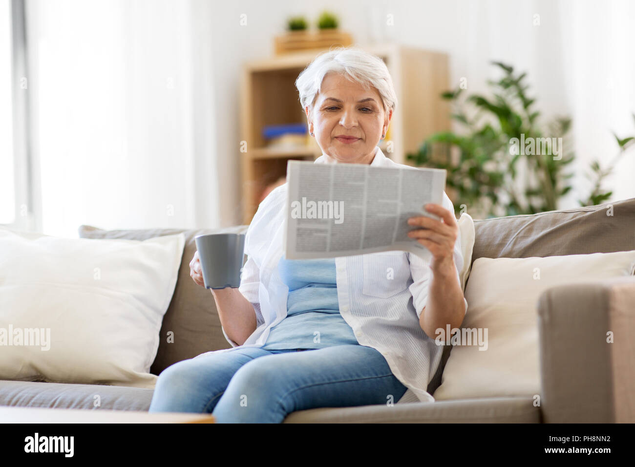 Senior donna con caffè quotidiano di lettura a casa Foto Stock