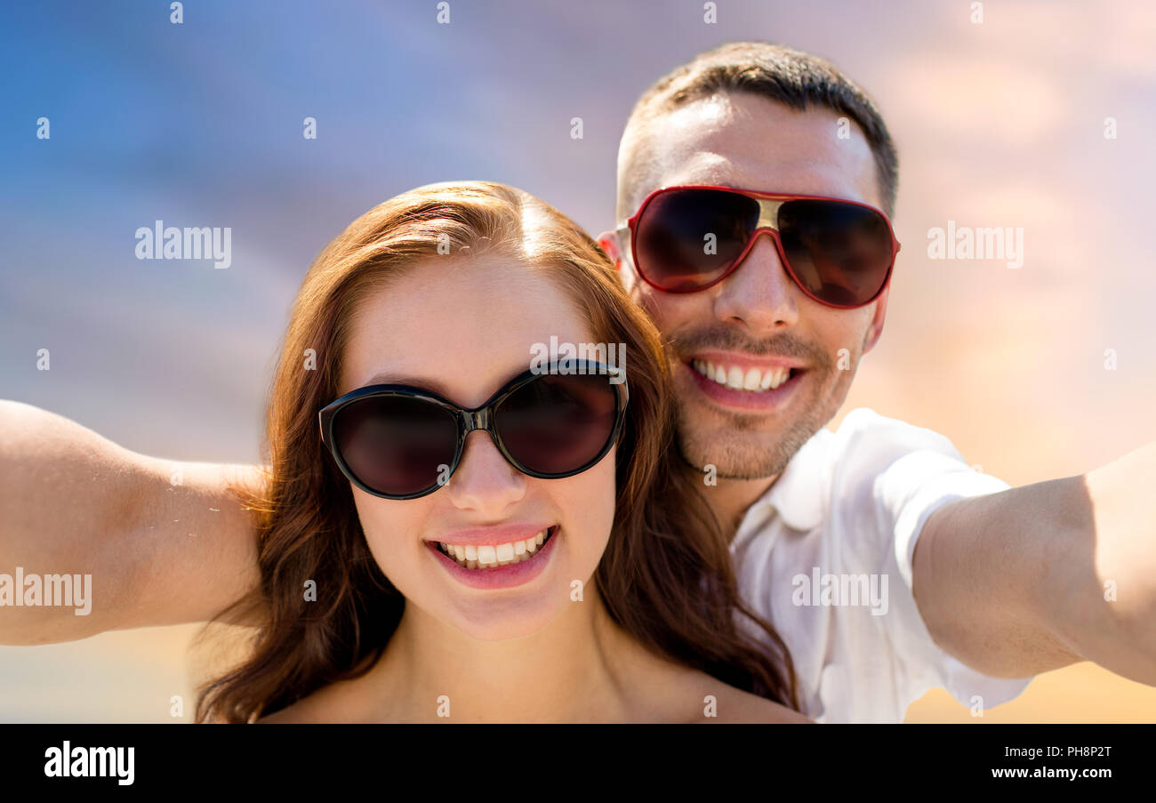Coppia sorridente indossando occhiali da sole rendendo selfie Foto Stock
