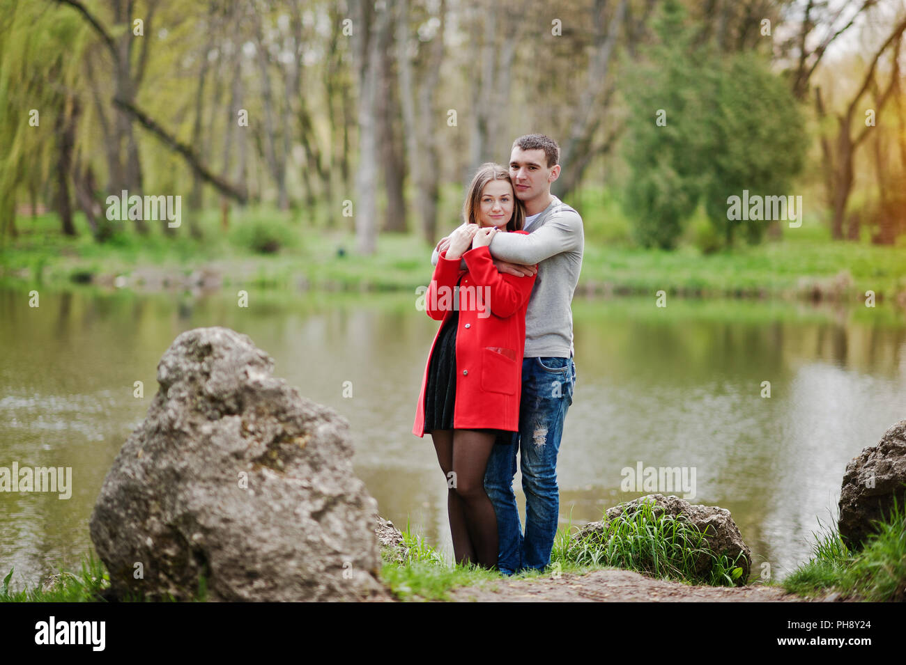 Felice di amare giovane soggiorno e abbracciando a sfondo parco lago Foto Stock