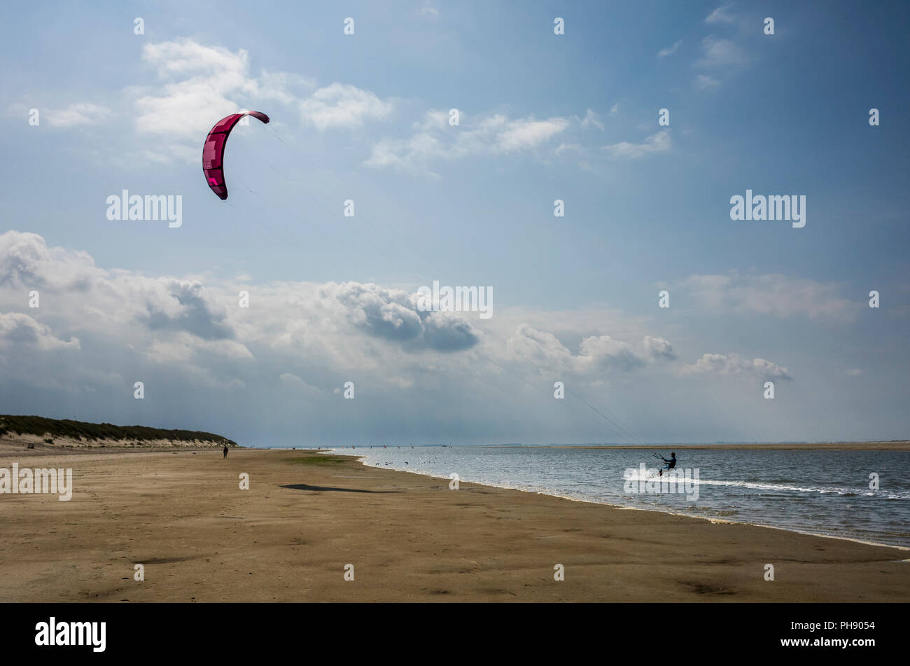 Am Strand Langeoog. Germania Deutschland. Una persona è kitesurf lungo il bordo dell'acqua della spiaggia di sabbia. Una stretta striscia di acqua di mare si estende lungo la spiaggia è ideale per gli sport acquatici. Fotografato su una luminosa giornata di sole principalmente con il cielo limpido ad eccezione di poche nuvole di luce. Foto Stock