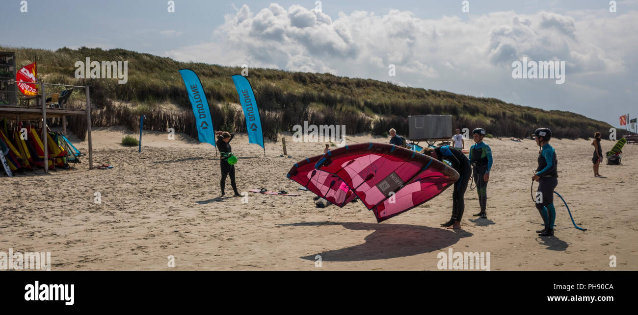 Am Strand Langeoog. Germania Deutschland. I giovani si preparano per saperne di kitesurf presso le associazioni turistiche scuola di surf. Essi sono già vestiti nei loro vestiti bagnati e gonfiare il kite della struttura di supporto. Si tratta di una luminosa giornata di sole. L ampia spiaggia è coperto di pulire la sabbia morbida che corre lungo la costa. Le dune di sabbia salgono sul bordo della spiaggia come si testa la navigazione. Foto Stock