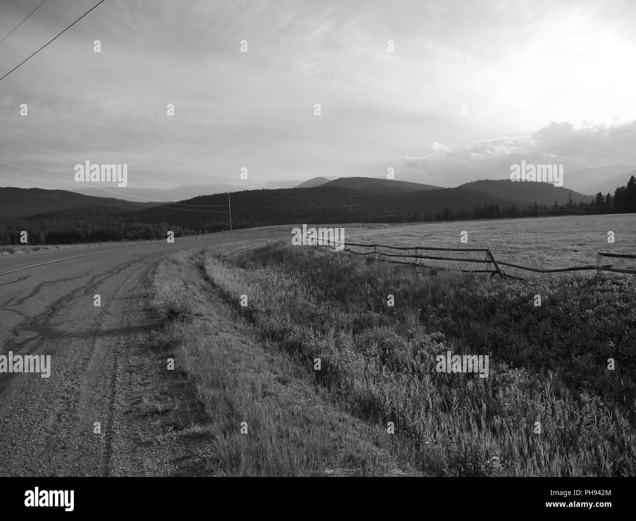 Terreni coltivati al tramonto in bianco e nero.una curva nel rurale Road in direzione di montagne distanti.un bel momento per fermarsi e godersi il Foto Stock