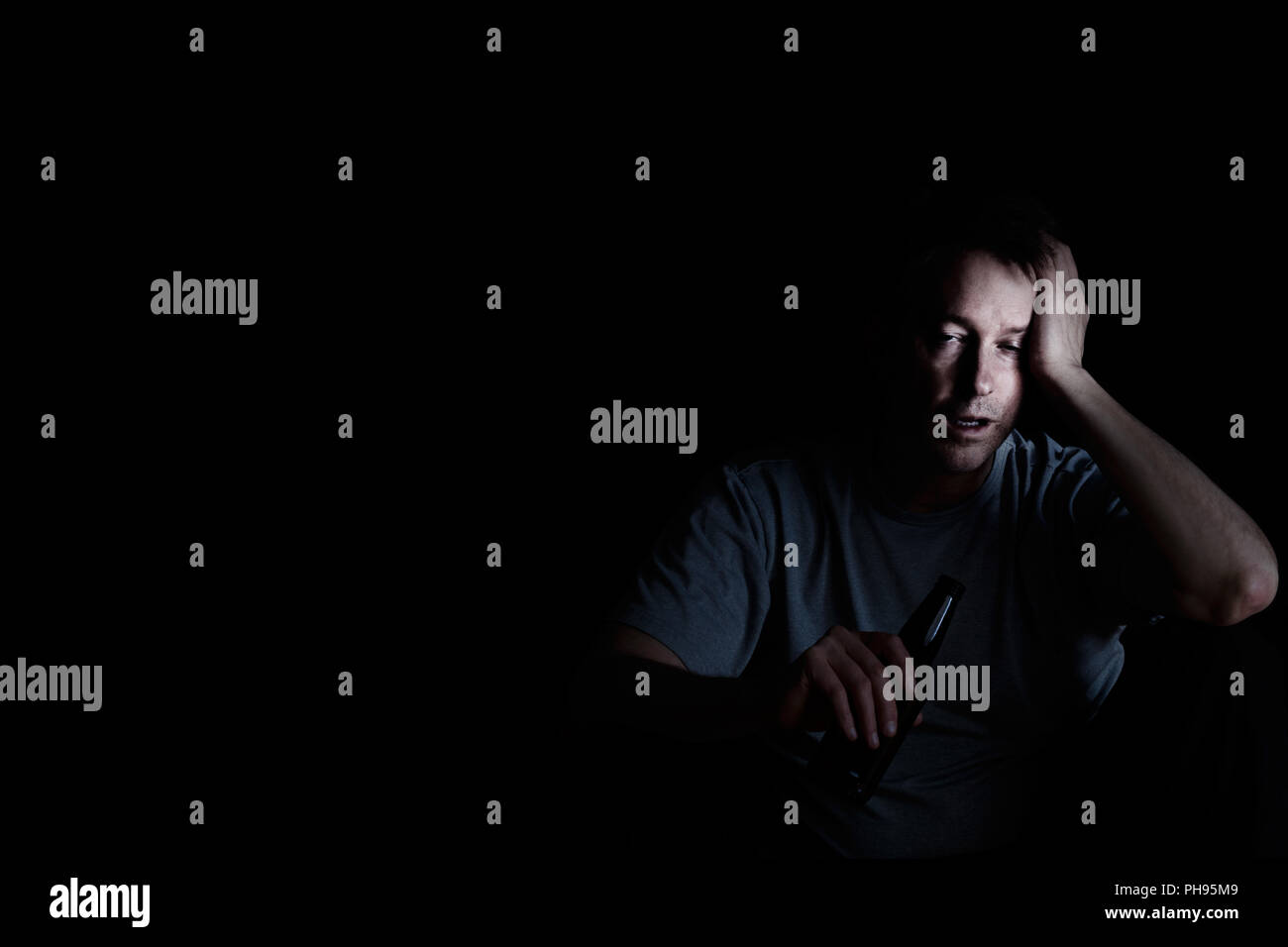 Uomo maturo la visualizzazione di depressione mentre si beve su sfondo scuro Foto Stock