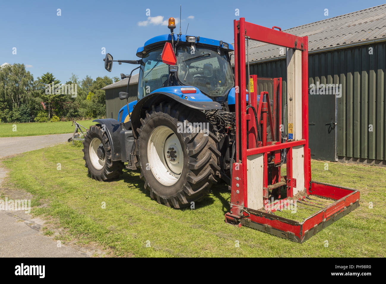 Trattore blu con un rosso affettatrice della balla Foto Stock