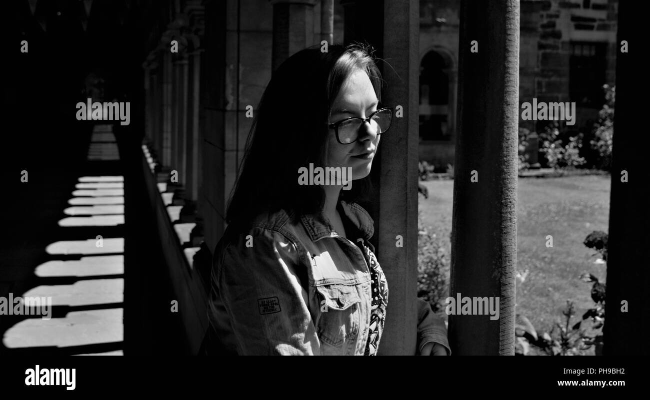 Ragazza staring blankly in un giardino di rose in una vecchia chiesa in Paisley, Scozia.in bianco e nero di una ragazza in piedi accanto al giardino di rose. Foto Stock