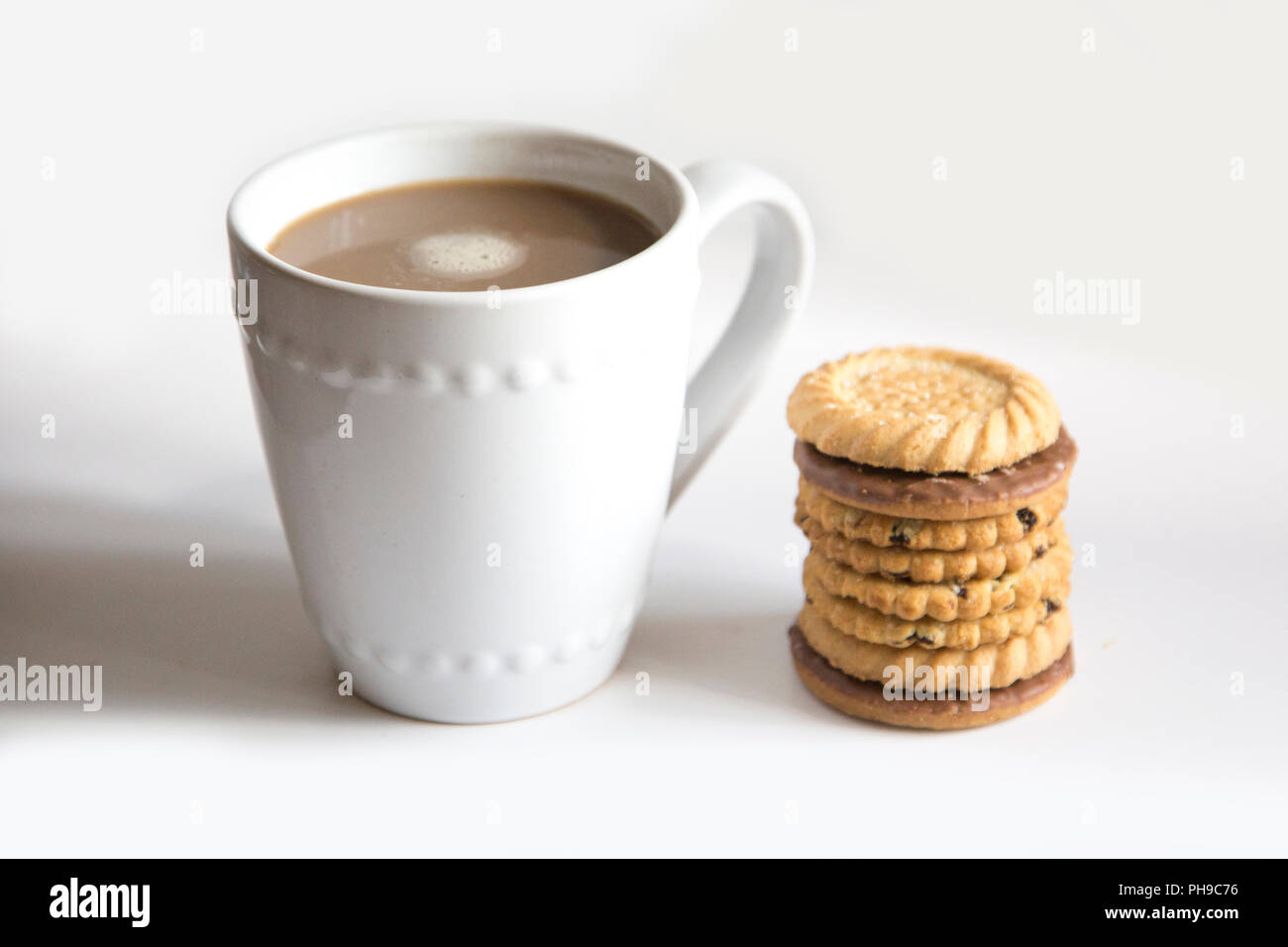 Una tazza di caffè in una tazza bianca su sfondo bianco con una pila di biscotti impilati accanto alla tazza Foto Stock