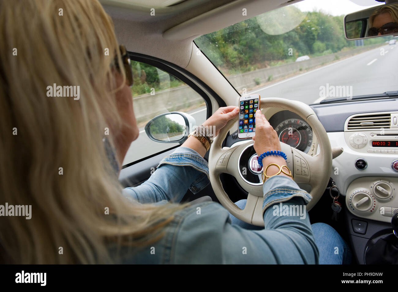 BOTTROP, Germania - 16 agosto 2018: una donna bionda sta verificando il suo smartphone mentre si guida su una strada in piena velocità. Foto Stock