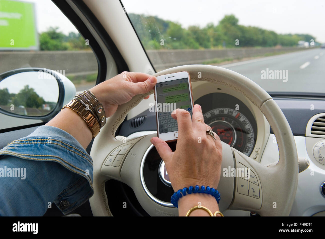 BOTTROP, Germania - 16 agosto 2018: una donna bionda è whatsapping sullo smartphone mentre si guida su una strada in piena velocità. Foto Stock