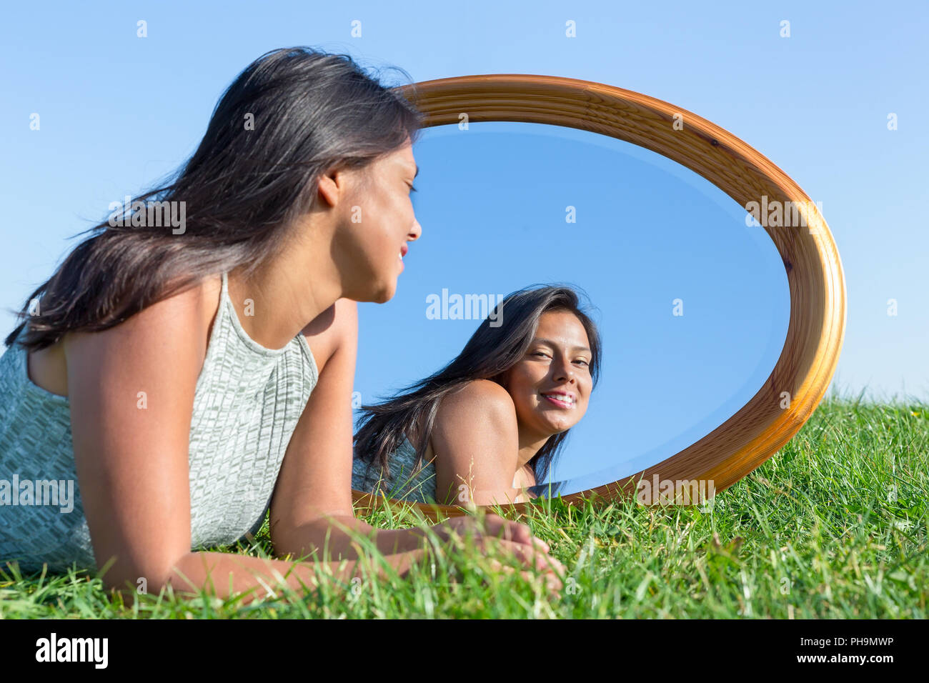 Donna sdraiata su erba esterno guardando in specchio Foto Stock