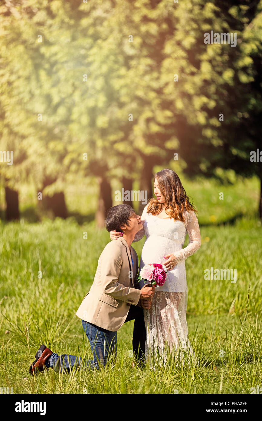 Futuro papà inginocchiato ad aspettarsi la mamma con fiori in mano Foto Stock