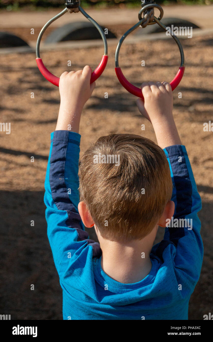 Un piccolo ragazzo con un blu camicia a maniche lunghe di tenere su anelli di metallo rosso con rivestimento in plastica su di essi Foto Stock