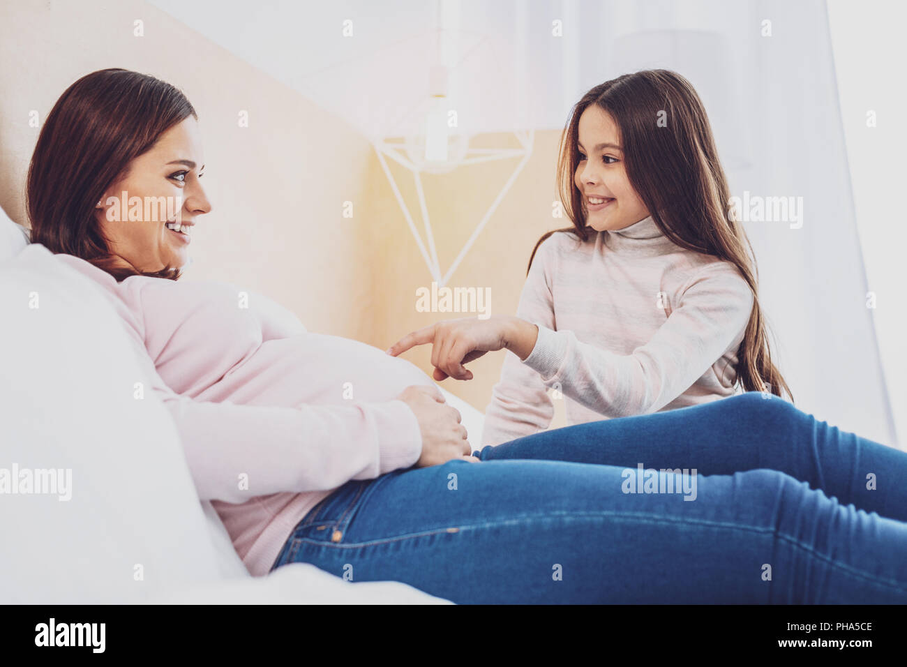 Curioso piccola figlia puntando al suo ventre delle madri Foto Stock