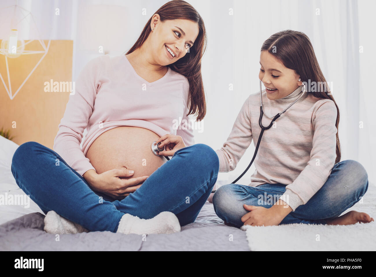 Lunghezza completa di entusiasta allegro figlia ascoltando il suo ventre delle madri Foto Stock