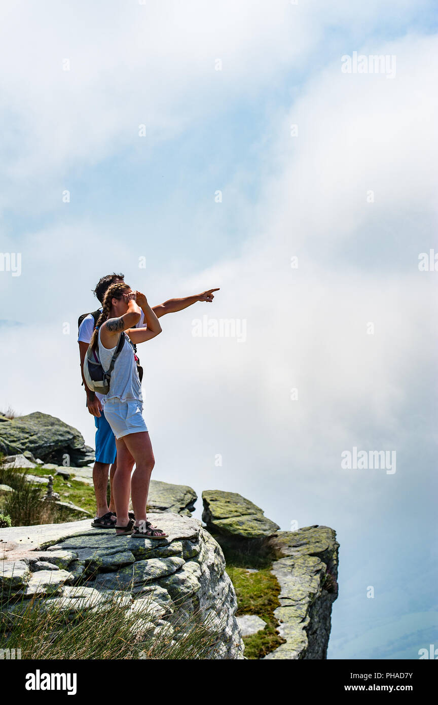 Un turismo giovane coppia con backpaks in piedi su una sommità di una montagna gode di vista di coperte da puffy nuvole bianche. Foto Stock