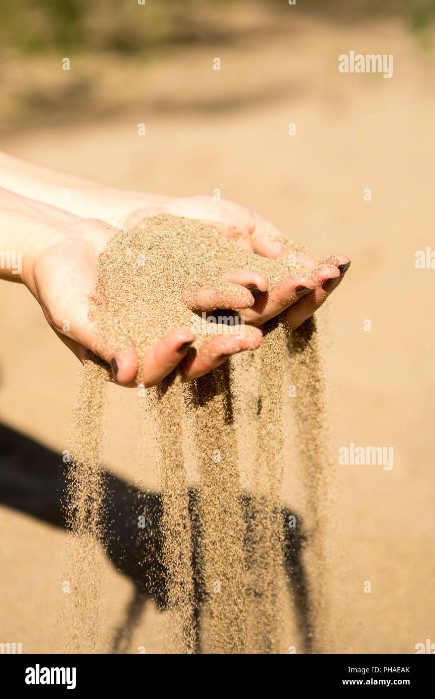 La sabbia che corre attraverso le mani della donna in spiaggia Foto Stock