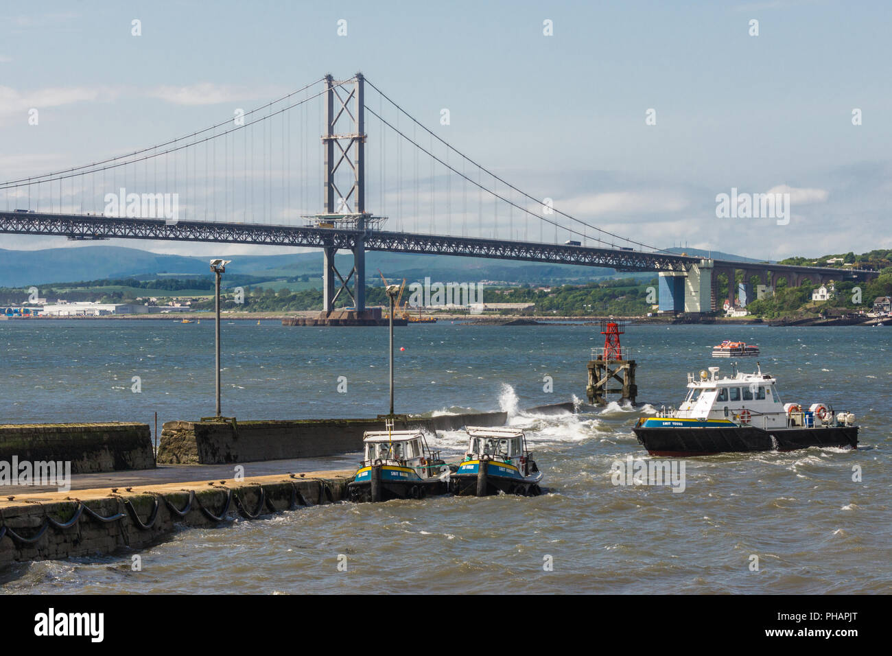 Queensferry, Scotland, Regno Unito - 14 Giugno 2012: Forth Road Bridge di sospensione su Firth of Forth tra il cielo blu e l'acqua. Pilota di Smit barche ormeggiate fino fr Foto Stock