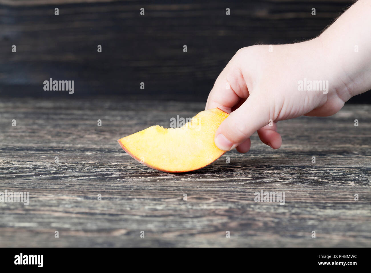 Un taglio fresco di pesche morbido su una tavola nera, close-up, una delle pesche è prelevato da un bambino Foto Stock