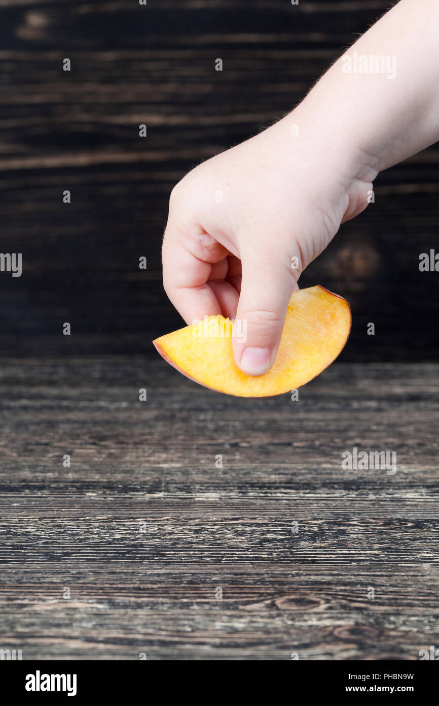 Un taglio fresco di pesche morbido su una tavola nera, close-up, una delle pesche è prelevato da un bambino Foto Stock