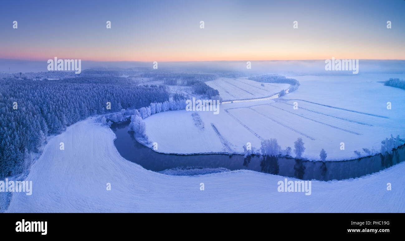 Paesaggio invernale vista da sopra. Antenna di scena invernale. Natale sfondo panoramico. Prato con fiume coperto dal bianco della neve. Foto Stock